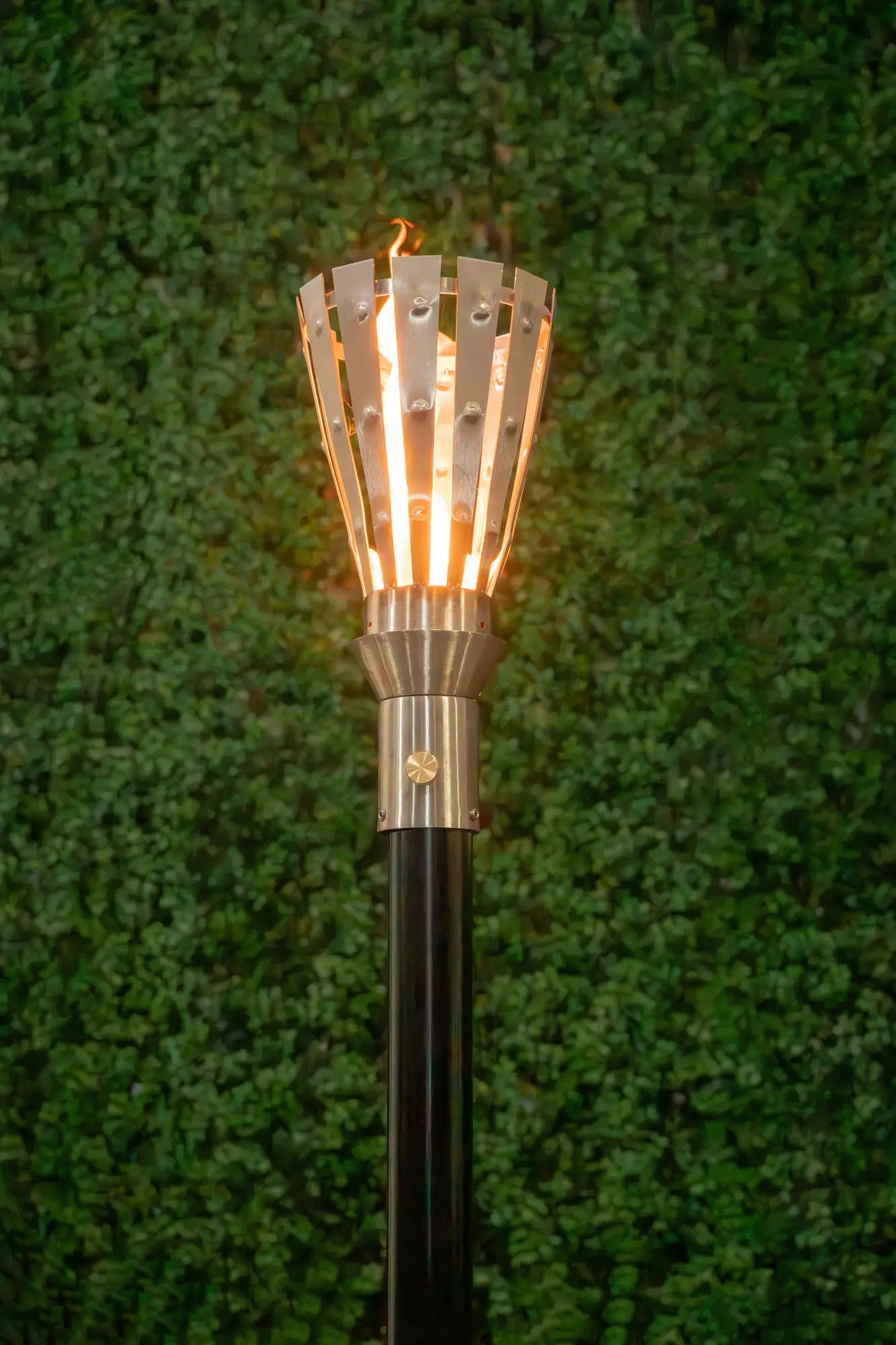 Torch with a metallic design on a green grass background. The Trojan Fire Torch by The Outdoor Plus is a striking, handcrafted outdoor accent inspired by ancient Greek design. Made from premium 304 stainless steel with rustic plate accents, it delivers a warm, elegant flame that enhances upscale patios, pool areas, or pathways. As part of a complete torch kit, it offers a thoughtful balance of beauty, function, and durability.