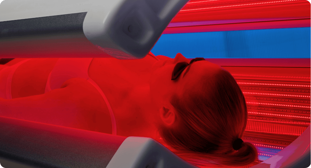 Person lying in a tanning bed with red light therapy equipment.